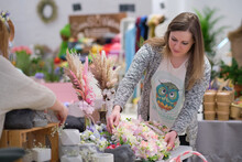 Business Owner Selling Behind Counter With Her Bouquet Of Dried Flowers At Local Market Of Craftsmen, Small Business. Young Woman Entrepreneur Sells Floral Holiday Composition.