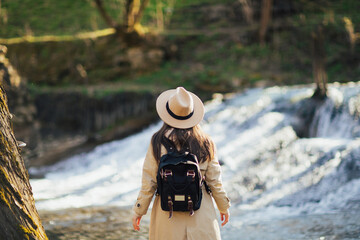 Wall Mural - Backside of woman with backpack and hat in forest on waterfall background. Travel concept.