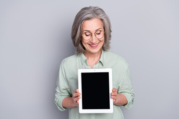 Sticker - Photo of happy smiling excited beautiful mature woman showing tablet display isolated on grey color background