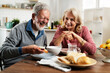© JustLife - Senior couple eating breakfast in the kitchen. Husband and wife talking and laughing while eating a sandwich.