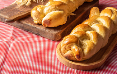 Homemade bread, two breads in the shape of a plait on wood and a red and white checkered tablecloth, a knife and a branch of wheat, selective focus.