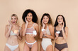 © LIGHTFIELD STUDIOS - amazed interracial women in underwear applying face cream on beige
