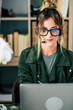 © simona - Modern pretty woman work at home in video conference call with laptop computer and headphone with microphone - online internet job in home office - content creator lifestyle female with glasses