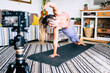 © simona - Young woman exercising at home doing pilates and recording at her with digital camera to teach workout and produce web class - content creator business free healthy lifestyle people concept