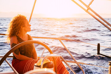 Wall Mural - Woman traveling by boat at sunset among the oceans - happy and free modern alternative lifestyle vacation female people sail at the sunset with ocean and sun in background