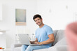 © BestForYou - Young smiling man in blue t-shirt with laptop in living room, freelancer