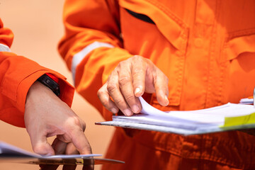 a worker in orange coverall uniform is opening documents to make a discussion on working procedure, 