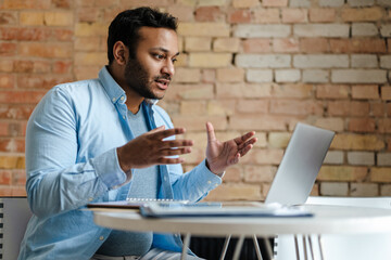 Middle eastern unshaven man gesturing while working with laptop