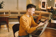 © Елизавета Старкова - Young smiling business man freelancer in casual yellow sweater and jeans working remotely using laptop and phone sitting in cafe, selective focus