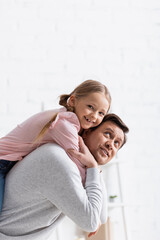 Wall Mural - smiling man piggybacking happy daughter at home