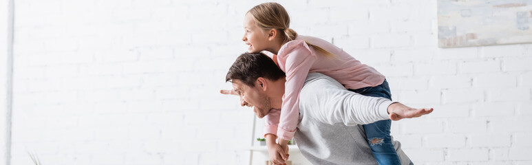 Wall Mural - side view of man piggybacking excited daughter at home, banner