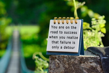 Motivational quote on white note with blurred background of hanging bridge