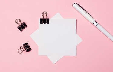 On a light pink background, black paper clips, a white pen and white note paper. Flat lay with copy space