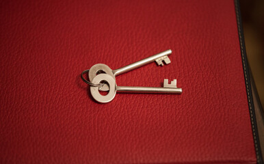 Two stainless steel keys on a key ring placed on a textured red leather bound book, closeup