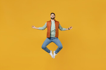 Wall Mural - Full length young caucasian man in orange vest mint sweatshirt glasses hold spread hand in yoga om gesture relax meditate try to calm down jumping higth isolated on yellow background studio portrait.