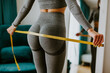 © shevtsovy - Fitness Woman Measuring body With Tape Standing In Front Of Mirror At Home. Beautiful woman checking success of weight loss program and measuring butt in front of mirror in living room. Slimming