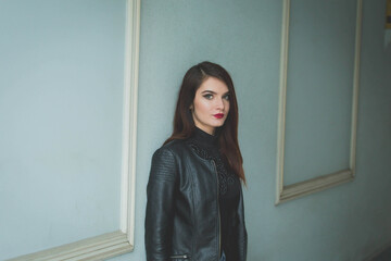 Poster - Young brunette female in a leather jacket posing in front of a wal