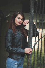 Poster - Young brunette female in a leather jacket posing in front of a gate