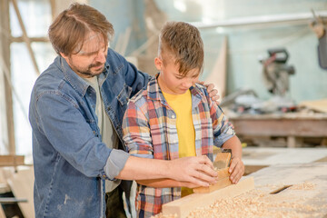 Wall Mural - Father teaches to young boy to plan wood in a carpentry workshop. Hobby and education concept