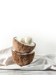 Two halves of coconut and coconut sweets on a wooden table .  Coconuts on a white napkin . Handmade coconut sweets with a copy space  .  Horizontal orientation picture with a coconut .