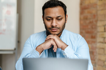 Middle eastern unshaven man working with laptop while sitting in office