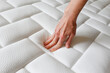 Cropped shot of young woman's hand testing white orthopedic mattress on firmness. Female pressing hypoallergenic foam mattress surface to check its softness. Close up, copy space, top view, background