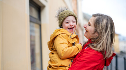 Wall Mural - Single mother holding down syndrome child outdoors in town, laughing.