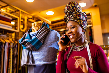tanzanian woman with snake print turban over hear working in fabrics shop calling to client by smart