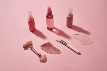 Rose quartz facial massage tools gua sha stone scrapers, face roller and beauty products in plastic bottles isolated on pink surface