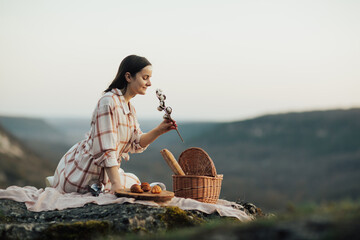 Wall Mural - Young woman sits on a rocky mountain at picnic with croissants and wine.