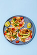Tacos with crispy fish, avocado, guacamole sauce and lime on blue background. Top view with copy space.