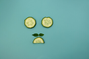 Wall Mural - Circles and semicircles of a cucumber with green mint leaves on a light blue background. Funny background.