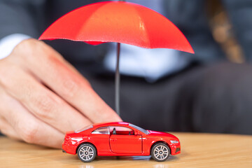 Wall Mural - Businessman hand holding umbrella cover or protection red car toy on table. Financial, money, refinance and Car insurance concept