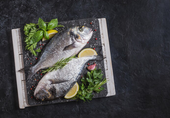 Raw fish with herbs and spices on black slate copy space food background.	