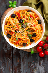 Sticker - Pasta with anchovies, olives, capers, garlic, and tomatoes in a plate on a dark wooden background. Italian food. Pasta alla puttanesca