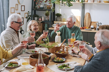 Group of happy senior people sitting at the table with glasses of red wine and having dinner at home