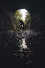 Silhouette Of A Young Cyclist On A Bicycle At The Exit Of A Tunnel. Via Verde De Loredo In Asturias, Old Railway Tracks Converted Into A Path. Silhouette Of A Person On A Bicycle, Sporty And Active.