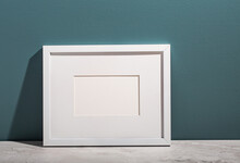 A White Picture Frame Leans On An Aegean Teal Painted Wall.