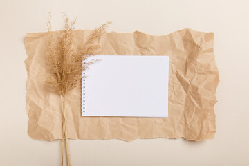 blank notebook with white paper and dry pampas grass on crumpled brown kraft-paper background. Mock-up invitation to-do planning list. Eco friendly natural creative layout. Flat lay composition 