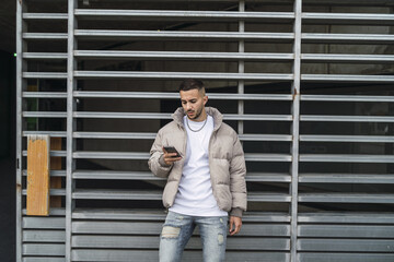 Poster - Stylish European man leaning on a gate and scrolling on his phone