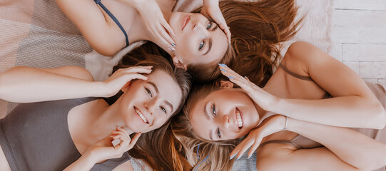 Women rest and have fun. Girlfriends laugh at home lying on the floor on pillows. Tree girls make homemade face and hair beauty masks. Women take care of youthful skin.