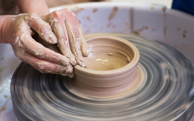 Women's hands make a plate of clay on a potter's wheel.