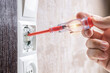 © Andrii - handyman repair wall light switch at apartment. worker using voltage electric tester pen to check power switch. electrician service concept