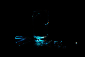 A broken drinking glass against a black background with different shards of glass reflecting at the base.