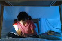 Asian Girl Child To Make A Camp To Play Imaginatively And Reading Book By Flashlight  In Living Room At Home..