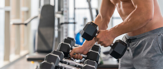 athletic bodybuilder man lifting dumbbell from rack in gym and fitness club