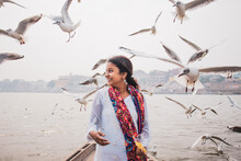 Smiling Indian Woman Looking To The Side On A Beach With Birds Flying Around Her