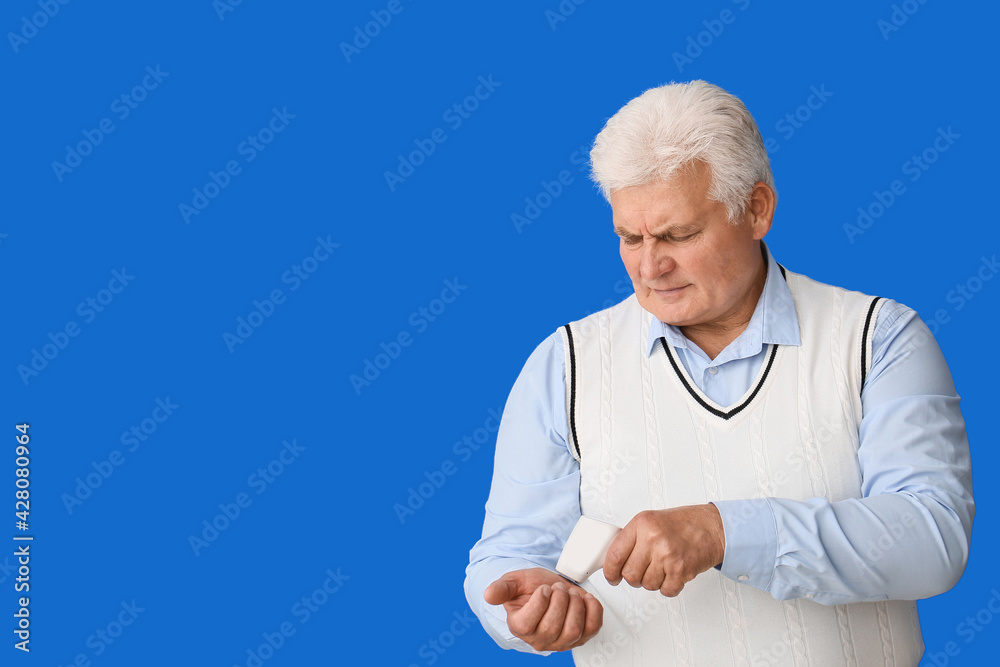 Senior man measuring his temperature on color background