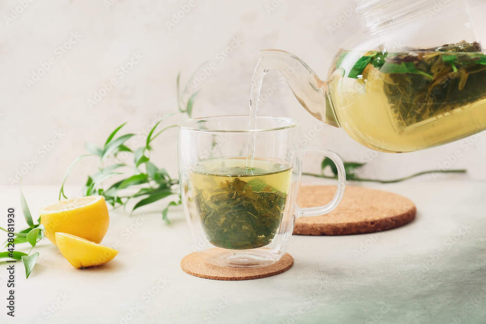 Pouring of green tea from teapot into cup on light background