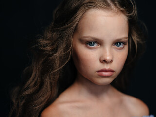 A beautiful blue-eyed girl with bare shoulders on a dark background and curly hair